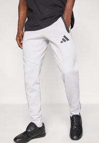 Γκρι αθλητικό παντελόνι με πλαϊνές τσέπες με φερμουάρ και μαύρες λεπτομέρειες. Διαθέτει εφαρμοστή γραμμή και μαύρο λογότυπο στο αριστερό πόδι.