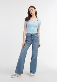 Lyseblå ribbet kortærmet top med krydsninger, parret med højtaljede lyseblå brede jeans og sneakers med grønne accenter.