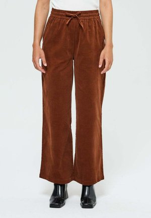 Pantalons larges en velours côtelé marron avec une taille élastique et un cordon de serrage. Tissu texturé ; portés avec des bottines noires.