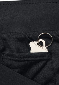 Pantalones de tela negra con una textura suave, que cuentan con un pequeño bolsillo delantero que sostiene un llavero y una etiqueta con borde ondulado.