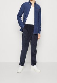 Navy button-up shirt, white tank top, and navy corduroy pants, paired with white sneakers. Smooth fabric, ribbed texture, and straight leg design.