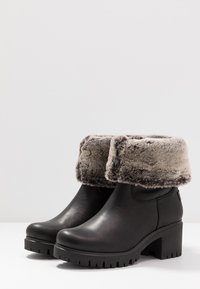 Črne usnjene gležnjarje zivi sivim umetnim krznenim robom, debelim peto in trdo podplatom z globokimi utori. Gladka površina in trdna zasnova.