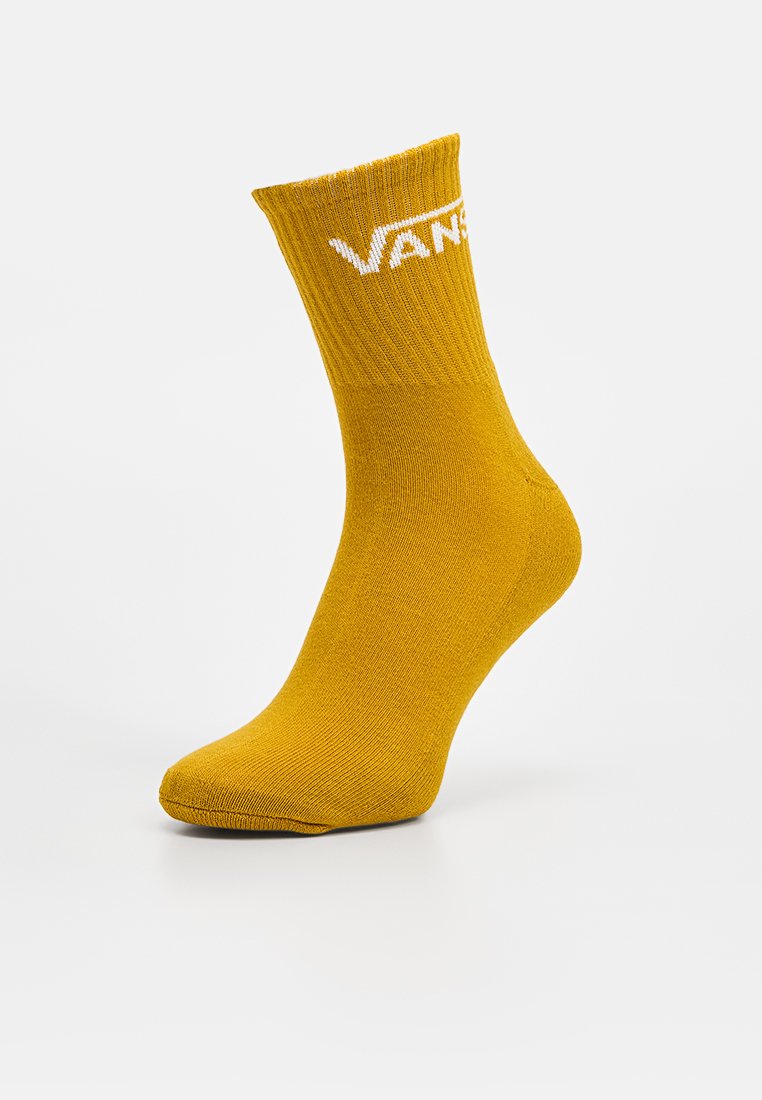 Calzino giallo senape fino al polpaccio con bordo a coste e logo bianco Vans nella parte superiore, esposto su un piede angolato.