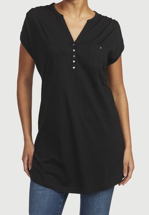Czarna bawełniana tunika z dekoltem w serek, krótkimi rękawami z podwinięciem i kieszenią na piersi. Posiada pięć srebrnych zatrzasków z przodu.