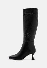 Botín de cuero negro hasta la rodilla con puntera afilada, tacón delgado y diseño minimalista, que cuenta con un zipper discreto y detalles de costura.