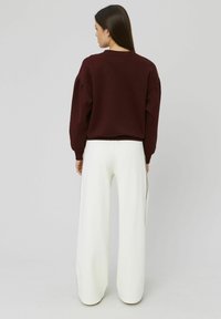 Sweatshirt court bordeaux avec épaules tombantes associé à un pantalon large blanc taille haute avec une bande latérale.