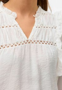 Witte katoenen blouse met een V-hals, gerimpelde kraag en horizontale kantdetails op de borst met een gestructureerde, gekreukte afwerking.