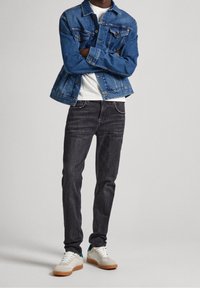En blå denimjacka med en klassisk design, tillsammans med mörkgrå jeans och vita sneakers med bruna sulor och teal-accenter.