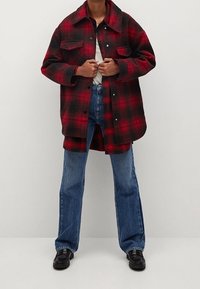 Rød og sort ternet flannel skjortejakke med to brystlommer, båret over en hvid t-shirt, parret med blå flagrende jeans og sorte sko.