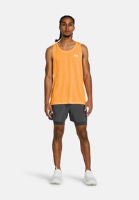 Orange tank top with a round neckline and white logo, paired with dark grey shorts. Model wears white athletic shoes.