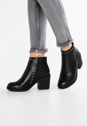Sorte ankelstøvler med sølvnitter, blokhæl og lynlås i siden, båret med grå skinny jeans med frynset kant.