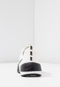 Valkoinen urheilukengä, jossa on teksturoitu verkkopinta, musta kantakoriste ja vetonauha, jossa on "NIKE"-teksti. Musta swoosh-logo sivussa.