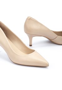 Zapatos de tacón de charol en color beige que presentan una punta afilada y un tacón de aguja de 5 cm. Textura suave con un escote bajo en el empeine y diseño minimalista.