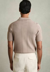 Polo din tricot cu m�ânecă scurtă, de culoare bej, cu dungi verticale, guler pliat și un design ajustat, asortat cu pantaloni de culoare deschisă.