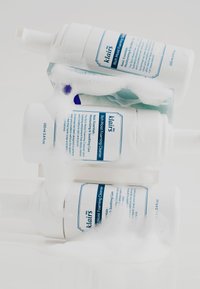 Trois bouteilles blanches de Klairs Rich Moist Foaming Cleanser empilées, partiellement immergées dans une mousse blanche, avec un texte bleu et un distributeur à pompe.
