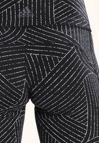 Leggings deportivos negros con patrones de rayas diagonales y verticales blancas, que presentan un ajuste ceñido y una tela suave y elástica.