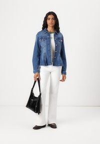 Denim jacket in medium blue with copper buttons, paired with a gray top, white flared pants, and a black leather handbag.