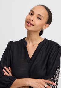 Blusa nera con texture, caratterizzata da un colletto a V e maniche a sbuffo con dettagli ricamati sulle пом.