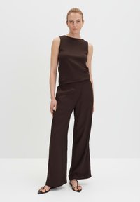 Brown ribbed sleeveless top paired with loose, flowy brown trousers. Both garments feature a soft texture and a minimalistic design.