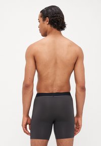 Čierne boxerské kraťasy s hladkým povrchom a elastickým pásom. Kraťasy majú strih do polovice stehen a sú priliehavé vzadu.