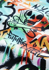 Barevný grafický textil s designem lebky, který obsahuje prvky graffiti v zelené, oranžové a černé barvě, na bílém pozadí s různými texturami.