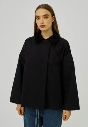 Black jacket with a corduroy collar, oversized design, and wide sleeves. Smooth texture, front closure, and subtle seams. Worn with jeans.