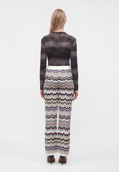 Femme aux longs cheveux blonds, de dos, portant un haut noir à motif en zigzag et un pantalon taille haute à motif en zigzag multicolore.