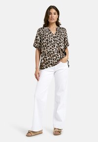 Bluse mit Leopardenmuster, kurzen Ärmeln und V-Ausschnitt, aus glattem Stoff. Kombiniert mit weißen weiten Hosen und beigen Sandalen.