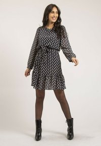 Robe à motif navy avec des manches longues, une ceinture à la taille et un ourlet froncé. Portée avec des bottines noires, présentant une texture lisse et un design moderne.
