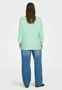 Mintunvihreä, löysä neulottu villapaita, jossa on ribbineulos ja pudotetut olkapäät, yhdistetty korkeavyötäröisiin, vaaleansinisiin leveälahkeisiin farkkuihin.