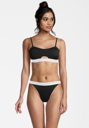 Set di bralette e perizoma neri con dettagli a taglio, realizzato in tessuto liscio. La bralette ha spalline sottili e una vita decorata con logo.