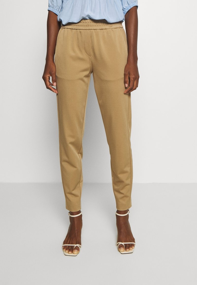 Beige byxor med elastisk midja och avsmalnande ben, med en slät yta och framfickor, matchade med ljusa, öppna sandaler.