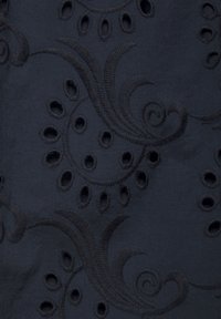 Laine bleu marine avec un motif de broderie florale texturée, présentant des tourbillons et des motifs découpés, créant un effet visuel en couches.