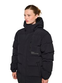 Kvinde iført en sort polstret vinterjakke med høj krave og hætte, der kigger til siden mod en hvid baggrund.