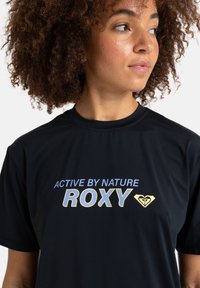 Camiseta deportiva de manga corta negra con el texto "ACTIVE BY NATURE" y "ROXY" en colores azul claro y amarillo, con un acento de logotipo de corazón.