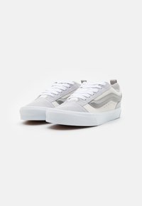 Graue und weiße Sneaker mit einem Obermaterial aus strukturiertem Stoff, flachen Schnürsenkeln und einer weißer Gummisohle. Sie verfügen über einen seitlichen Streifen und durchbrochene Akzente.
