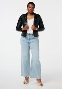 Veste de moto en cuir noir avec fermeture éclair, haut crème, jean ample bleu clair et sandales à talons carrés beiges.