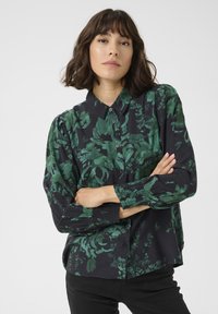 Long-sleeve black shirt with green floral pattern, button-down front, and gathered detail at cuffs. Smooth fabric with a relaxed fit.