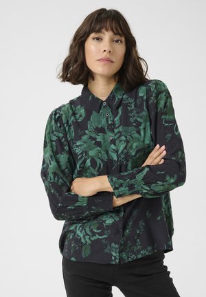 Camicia nera a maniche lunghe con motivo floreale verde, con chiusura a bottoni sul davanti e dettaglio arricciato sui polsini. Tessuto morbido con una vestibilità comoda.