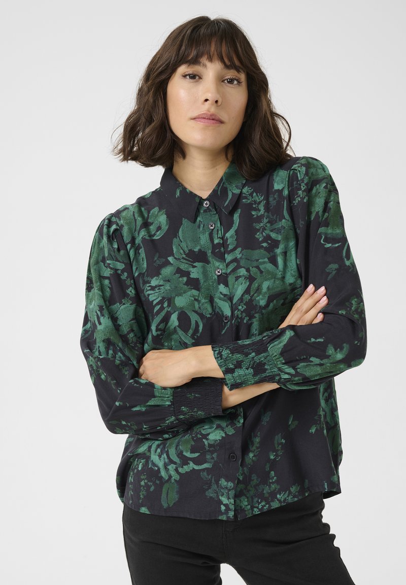 Long-sleeve black shirt with green floral pattern, button-down front, and gathered detail at cuffs. Smooth fabric with a relaxed fit.