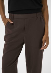 Bruine op maat gemaakte broek met een elastische tailleband, zijzakken en een gladde textuur, met een rechte pijpdesign.