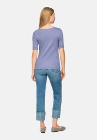 Lavendel Kurzarm-Top mit Boots-Ausschnitt, kombiniert mit hellblauen umgeschlagenen Jeans und grauen Ballerinas. Klare Linien und weiche Textur.