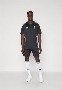 Black athletic jersey with short sleeves, featuring teal logo and accents, paired with black shorts and white socks with black stripes, worn with cleats.