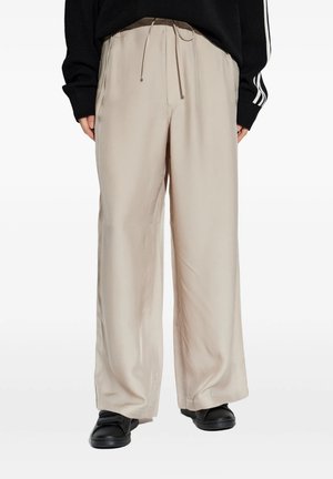Persona che indossa pantaloni beige larghi e comodi con coulisse in vita, maglione nero con strisce bianche e scarpe nere.