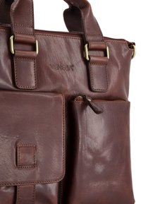 Brun læder håndtaske med en tekstureret overflade, der har to håndtag, en lynlåslukning på toppen, og en yderlomme med lynlåslukning.