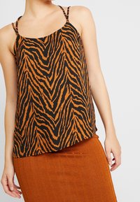 Top sin mangas de patrón negro y naranja con tirantes finos, que presenta un diseño de rayas de tigre en zigzag. Fabricado con una tela ligera y texturizada.