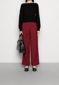 Czarny dziany sweter z szerokim dekoltem, bordowe wysokie spodnie z plisami, czarna torebka i czarne buty z kwadratowym noskiem.