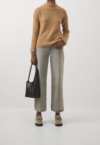 Beiger Rippstrickpullover, hellgraue weite Jeans, schwarze Schultertasche und beiger Schuh mit Schlangenledermuster und taktilen Akzenten. Sauberer, moderner Stil.