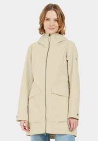 Parka imperméable beige avec fermeture éclair, capuche réglable, deux grandes poches avant et coupe décontractée. Texture lisse, design minimaliste.