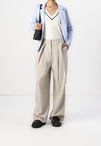 Ljusblå skräddarsydd kavaj, vit topp med scalloped halsringning och svarta detaljer, beige plisseradebyxor och kraftiga svarta skor.